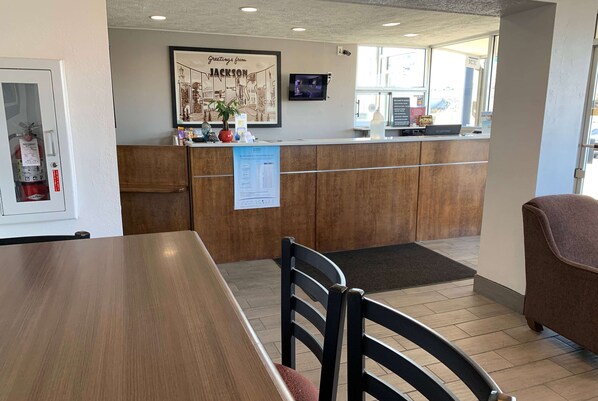 Un área de recepción con mostrador de madera, un extintor, un cartel de bienvenida enmarcado y una pantalla digital.