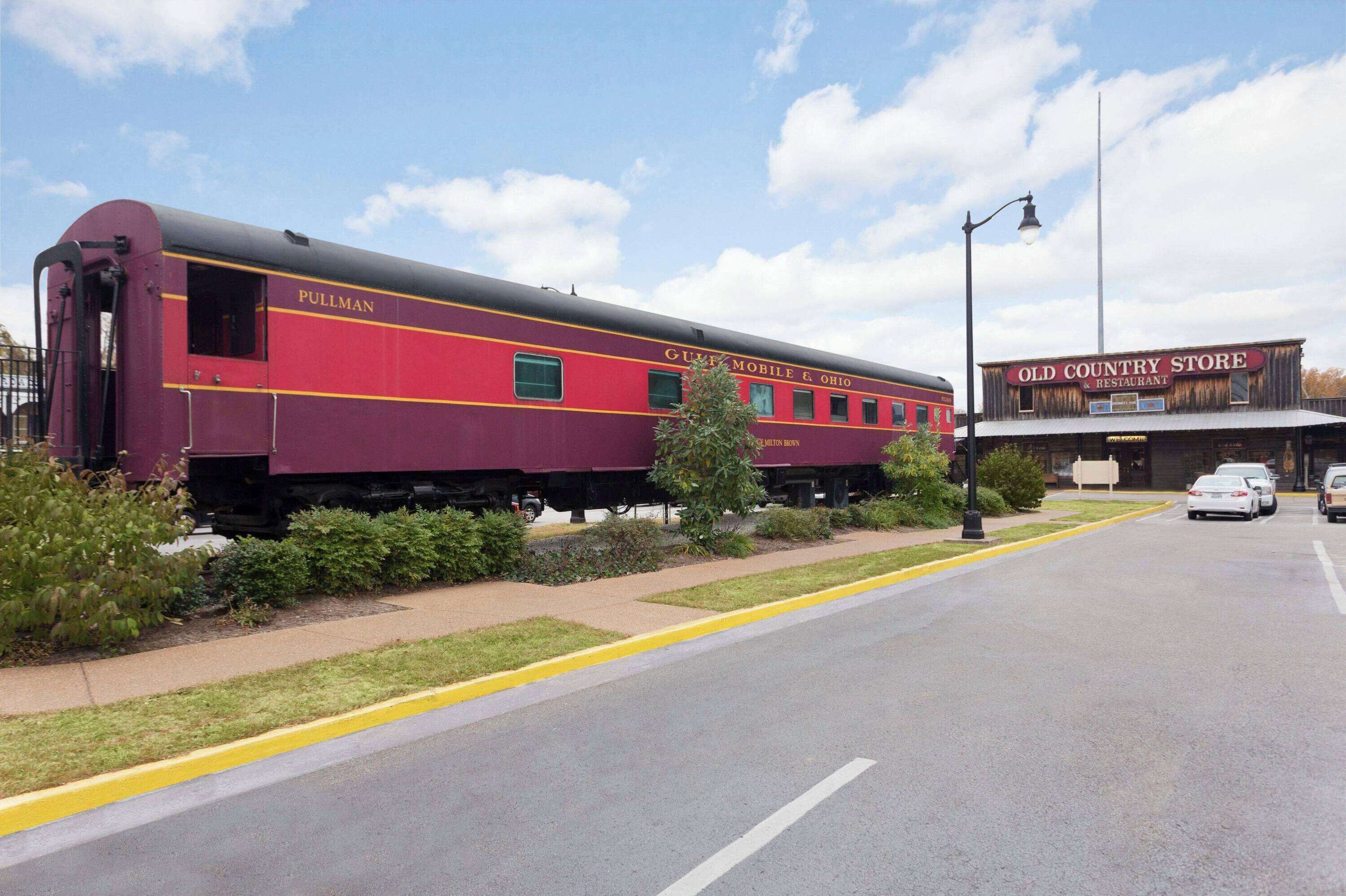 Un wagon-lit Pullman est garé au bord d’une route, avec une vieille boutique de produits régionaux en arrière-plan.