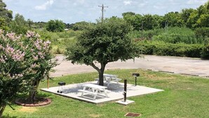 A picnic area with a tree, benches, and a grill. - Motel 6 Clute, TX (Clute)