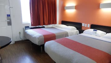 Una habitación de hotel con dos camas, un escritorio y un ventanal con cortinas.