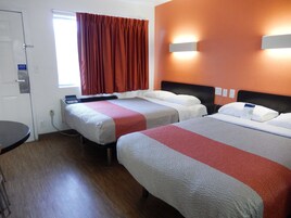 Una habitación de hotel con dos camas, un escritorio y un ventanal con cortinas.