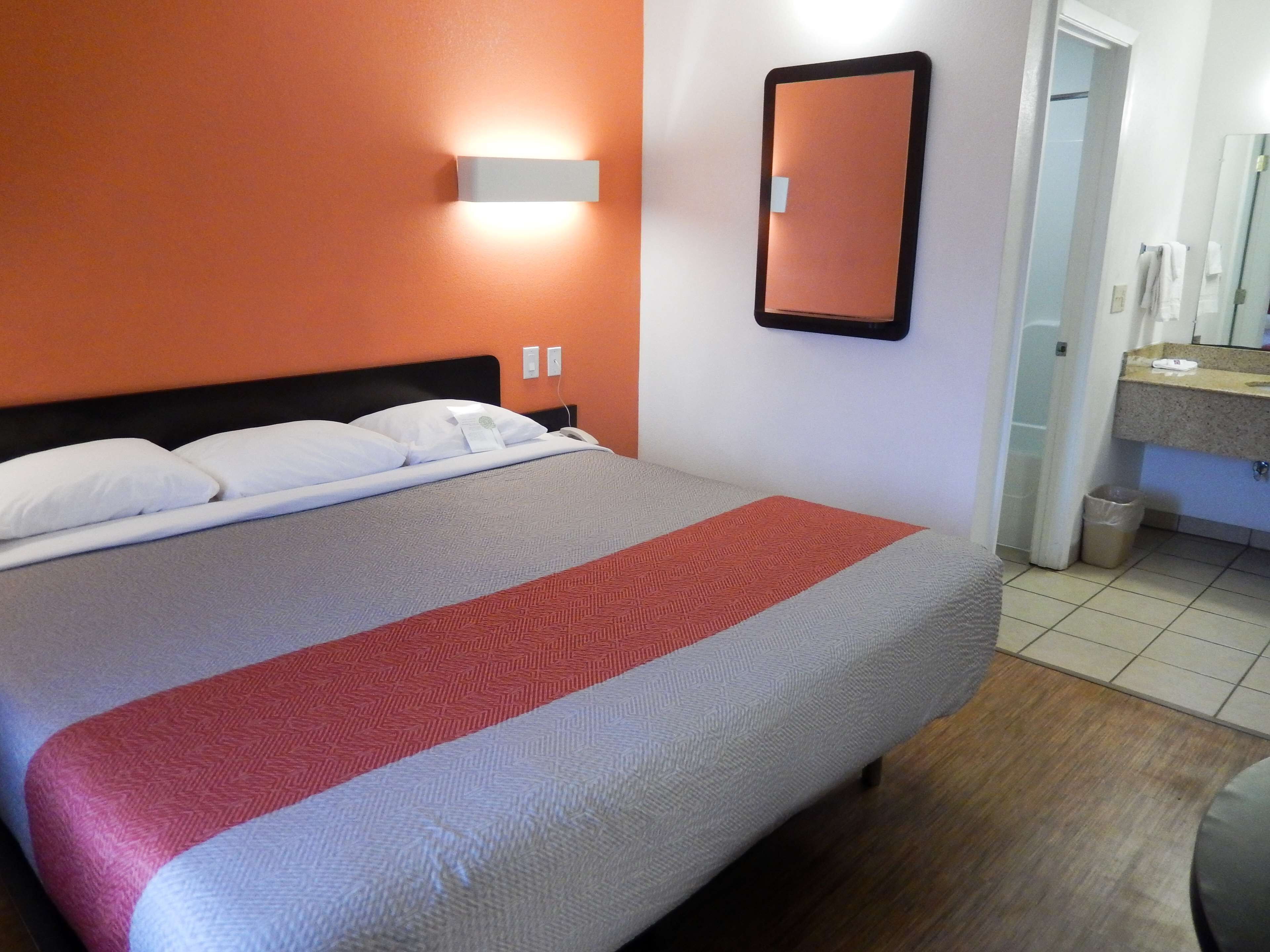 Habitación de hotel con una cama, una mesita de noche, un espejo montado en la pared y un baño visible a través de una puerta abierta.