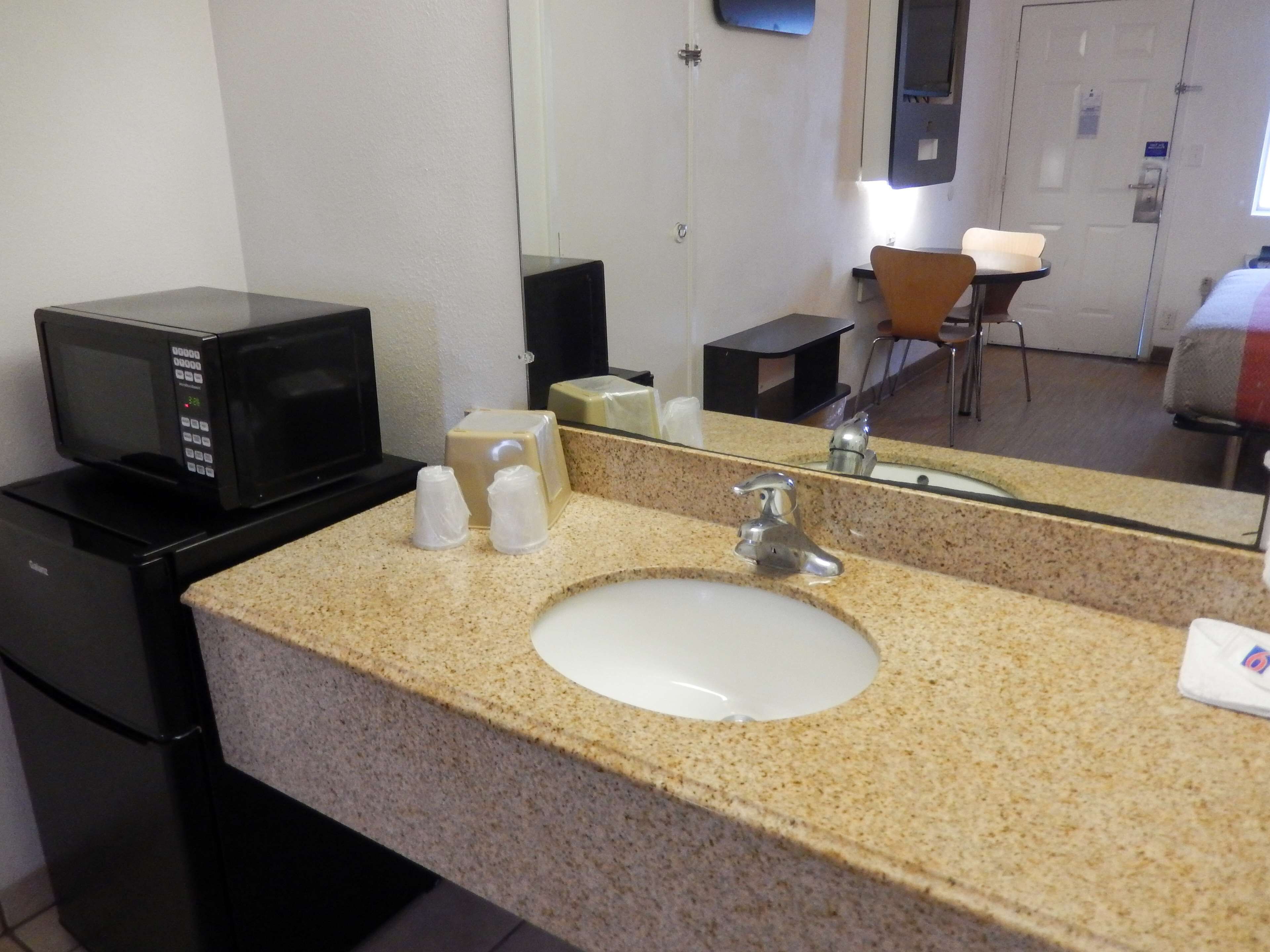 A hotel bathroom with a sink, mirror, and a microwave on the countertop.