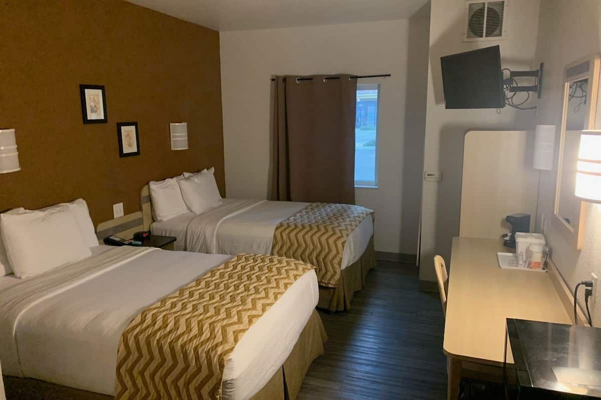 Quarto de hotel com duas camas, uma escrivaninha, uma cadeira, televisão e janela com cortinas.