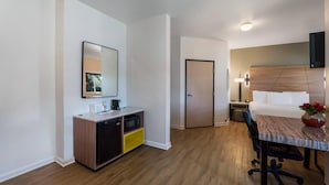 A hotel room with a bed, a desk with a chair, a small kitchenette, a door, and a mirror on the wall. - Quality Inn Yuba City/Marysville (Yuba City)