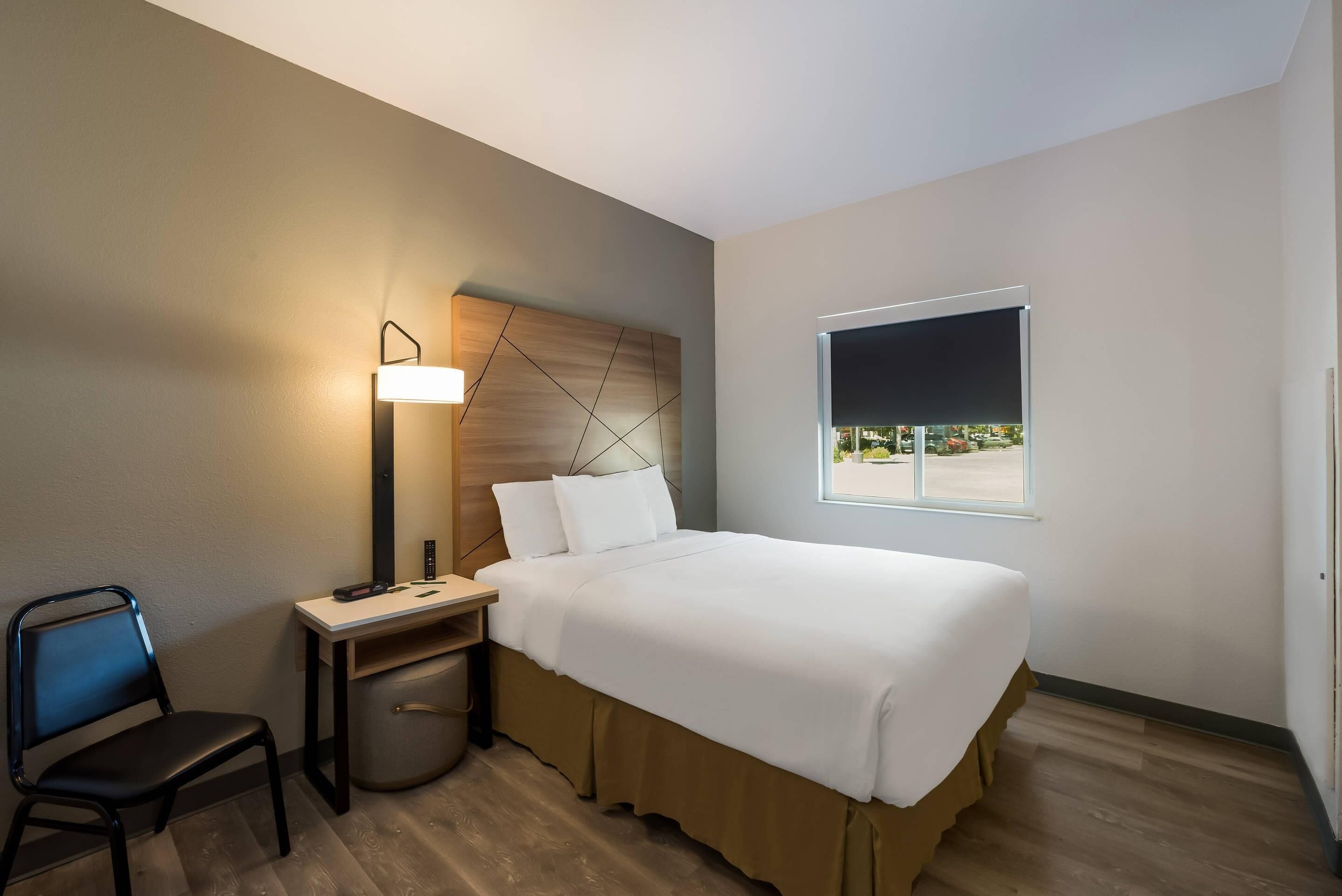 A hotel room with a bed, a desk with a lamp, a chair, and a window with a view.