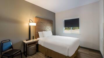 A hotel room with a bed, a desk with a lamp, a chair, and a window with a view.