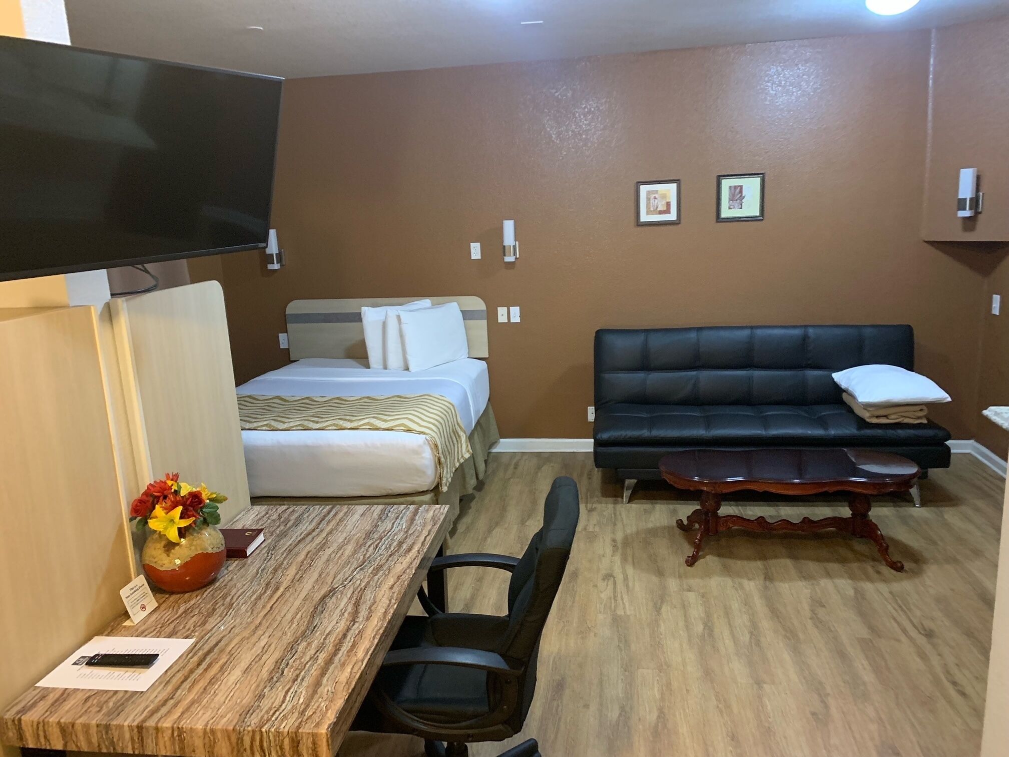Una habitación de hotel con una cama, un sofá de cuero negro, una mesa de centro de madera y un escritorio con una silla.