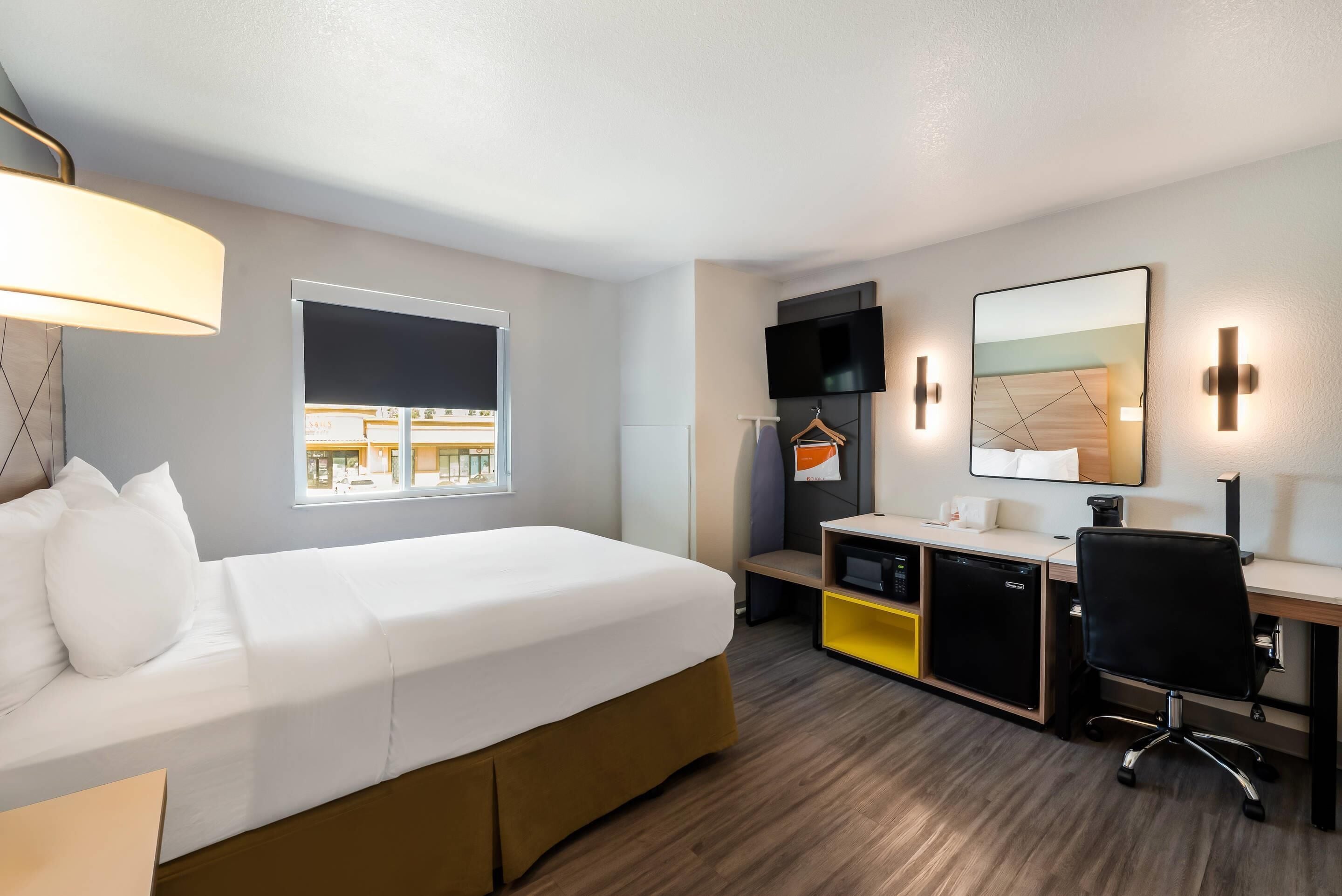 A hotel room with a bed, desk, chair, TV, and a window with a view.