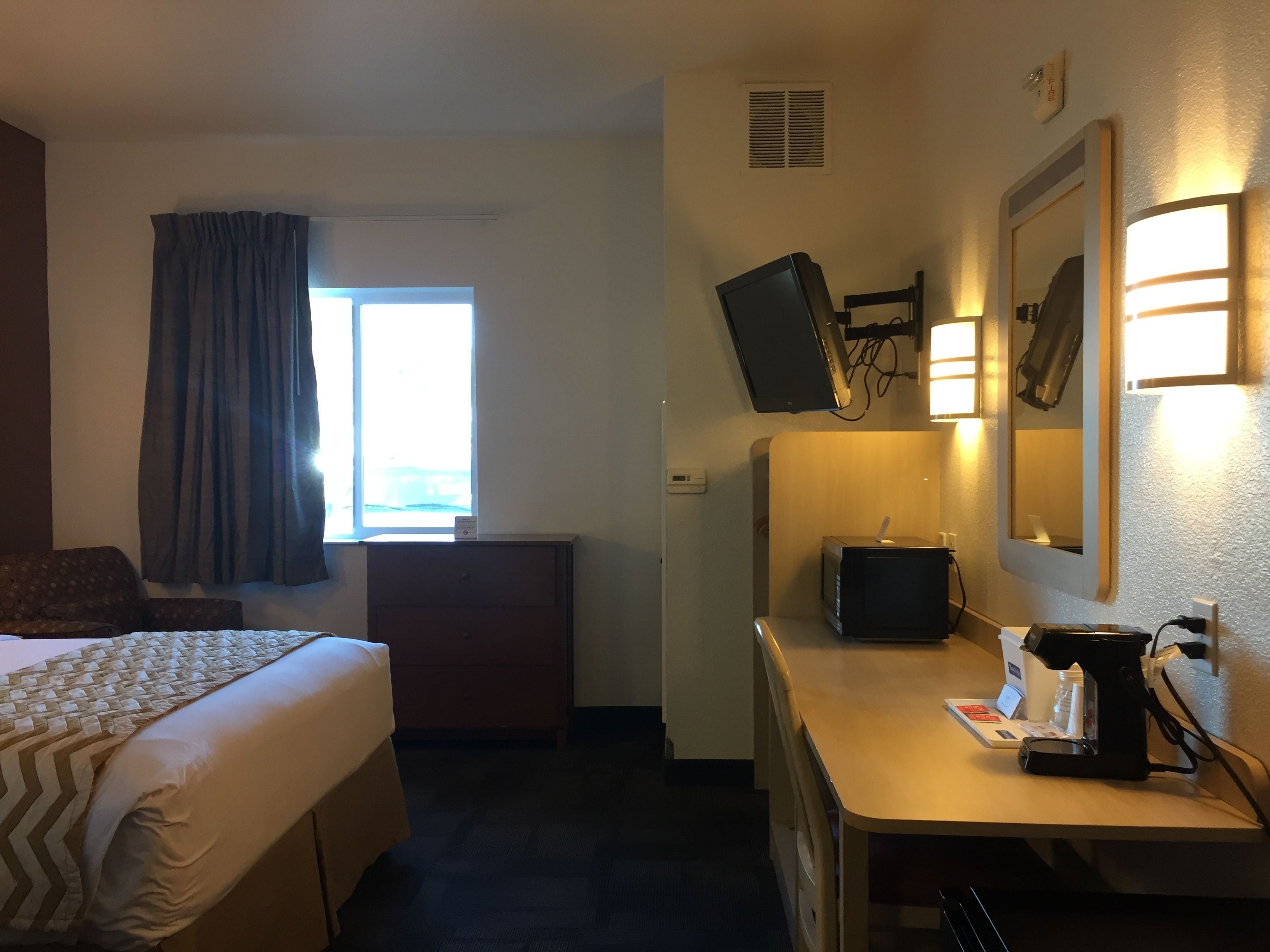 A hotel room with a bed, a desk, a TV, and a window with curtains.