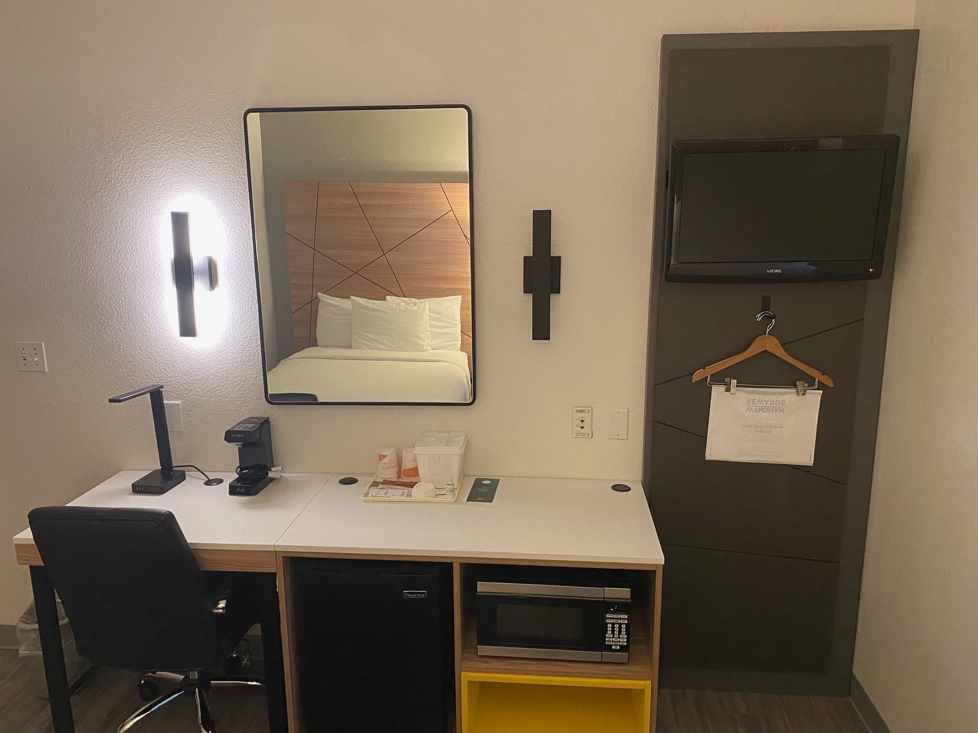 Habitación de hotel con escritorio, espejo, televisión, microondas y un pequeño armario.