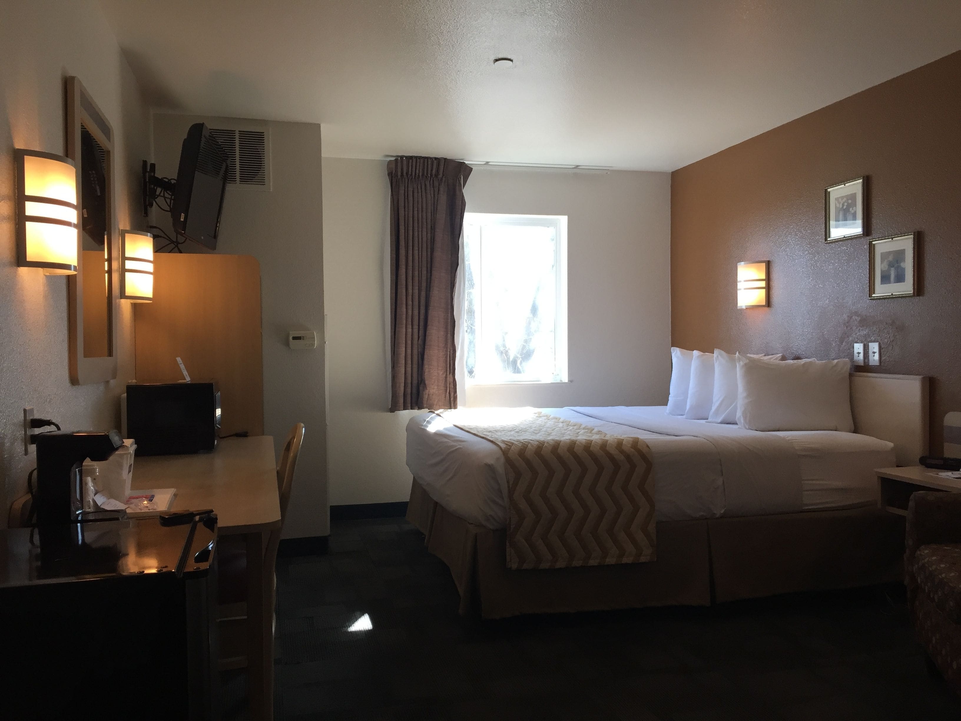 Een hotelkamer met een bed, nachtkastje, bureau, stoel en een raam met gordijnen.