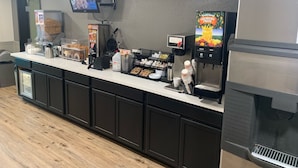 A counter with a coffee machine, a TV mounted on the wall, and a juice dispenser. - Quality Inn Yuba City/Marysville (Yuba City)