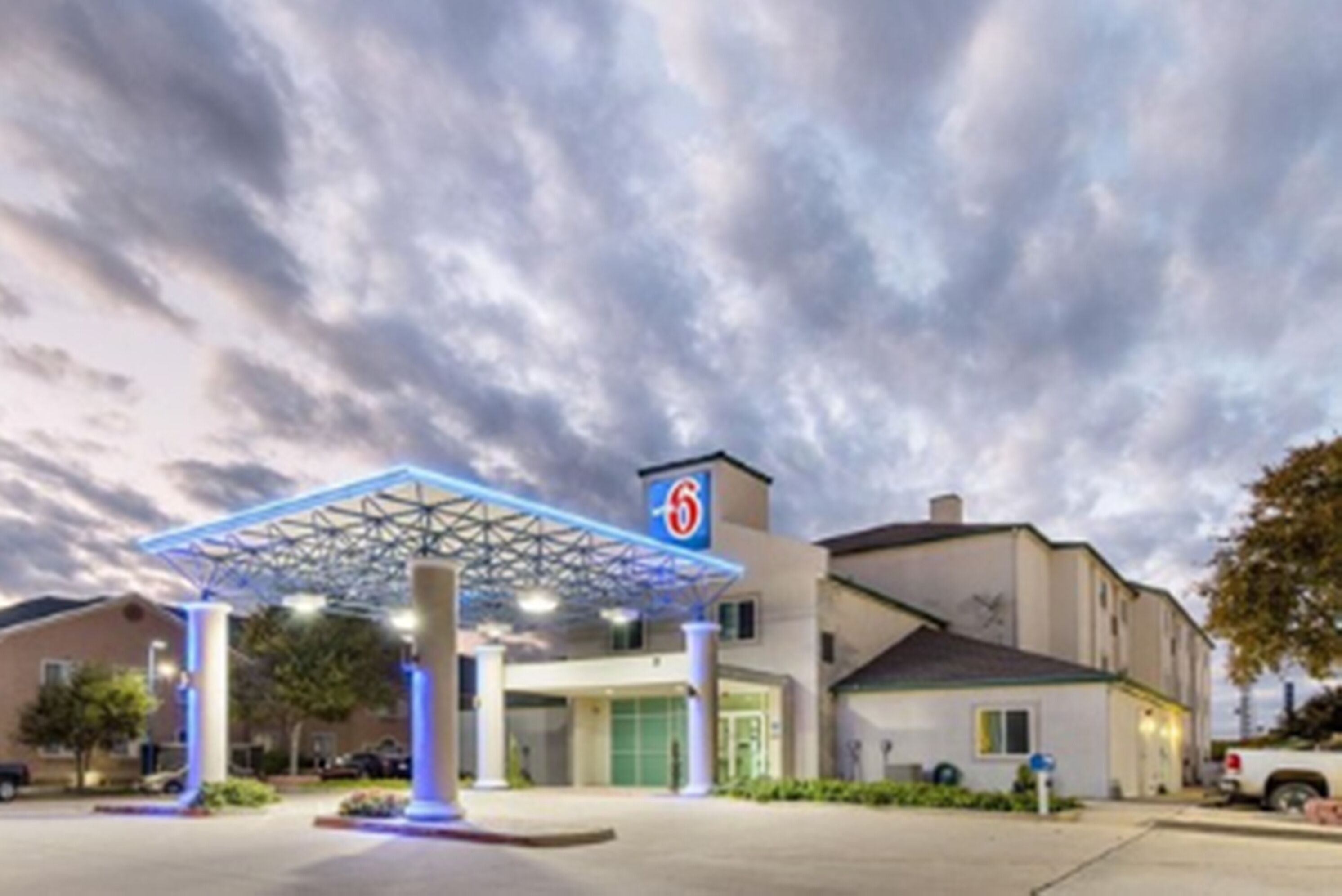 Un motel con un llamativo toldo azul, un cartel grande con el número 6 y un estacionamiento.