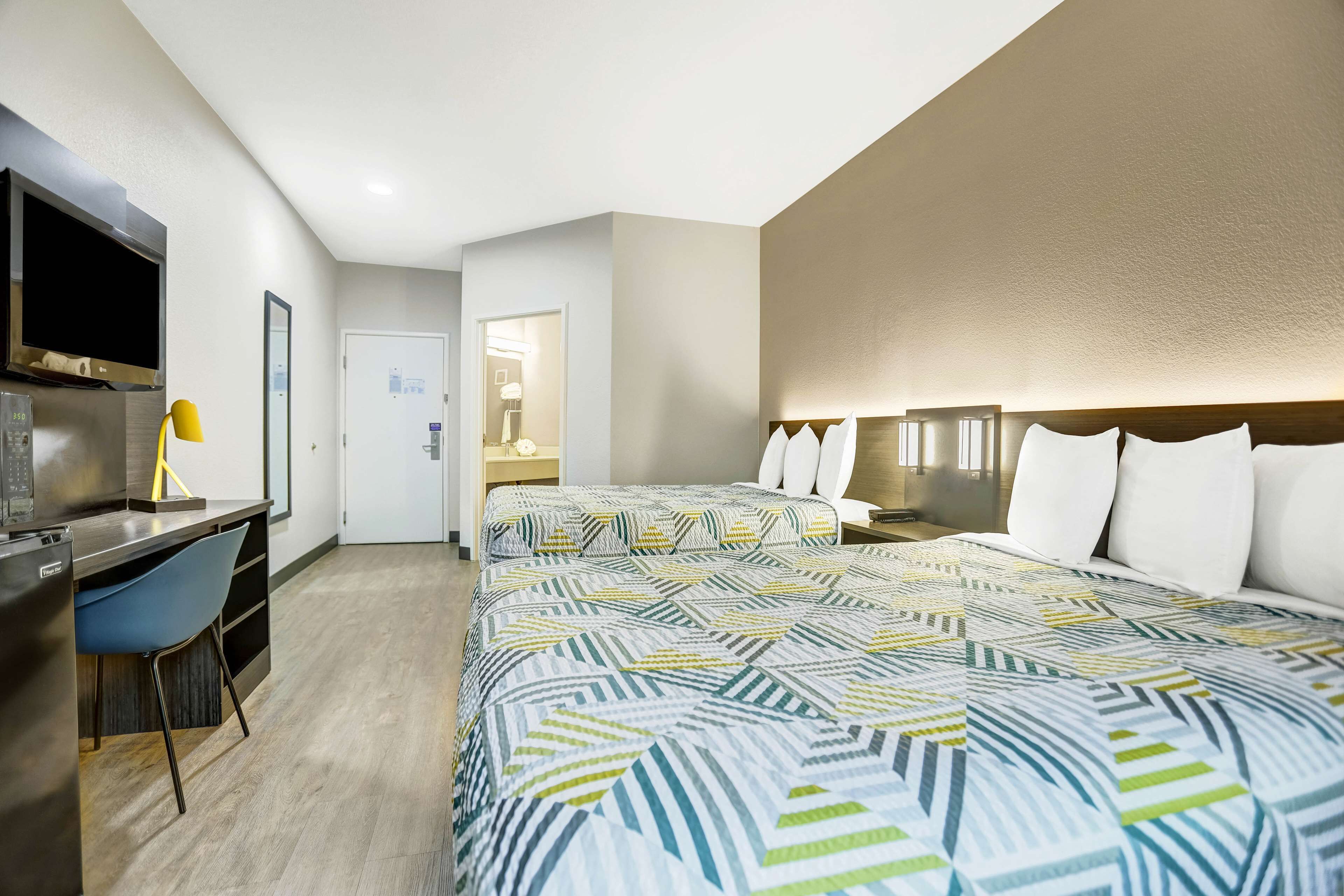 A hotel room with a bed, a desk, a chair, a TV, and a mirror.