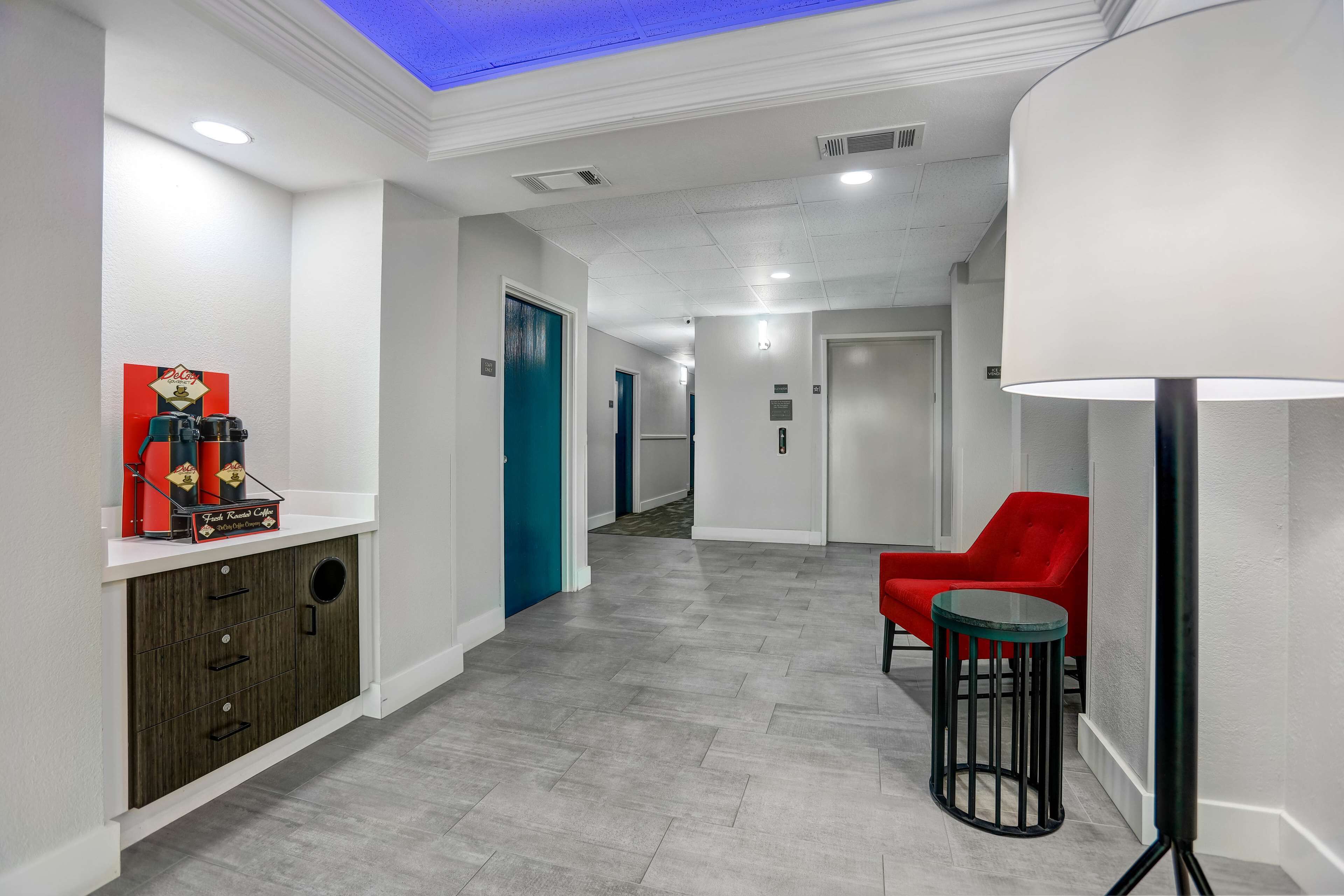 A modern hallway with a white reception desk, a red chair, and a floor lamp.