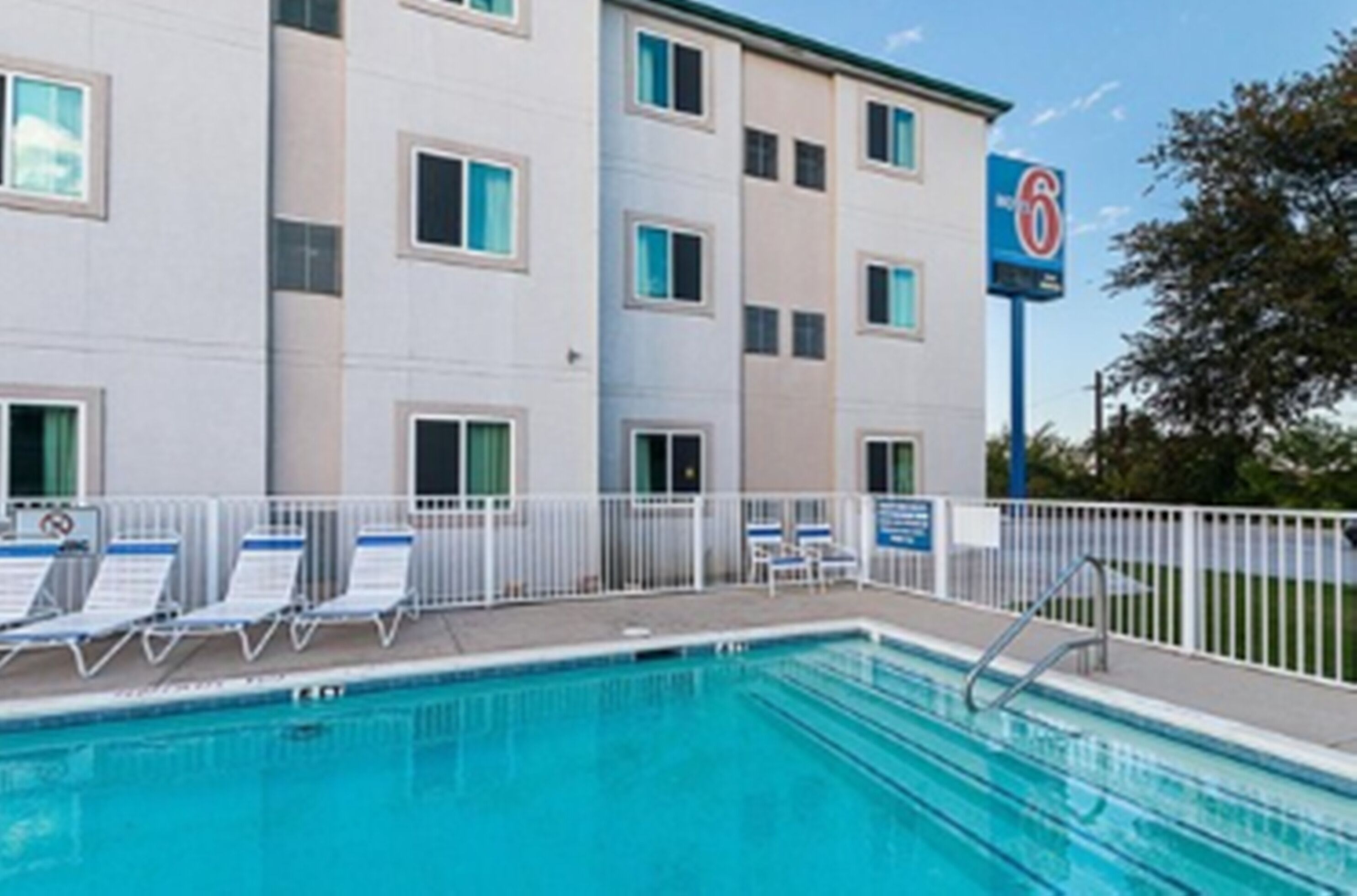 A hotel with a swimming pool, a sign indicating a 6-star rating, and a fenced area with lounge chairs.