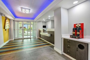 Zona de recepción de un hotel con diseño moderno, que incluye una alfombra colorida a rayas, un mostrador de recepción y una estación de café.