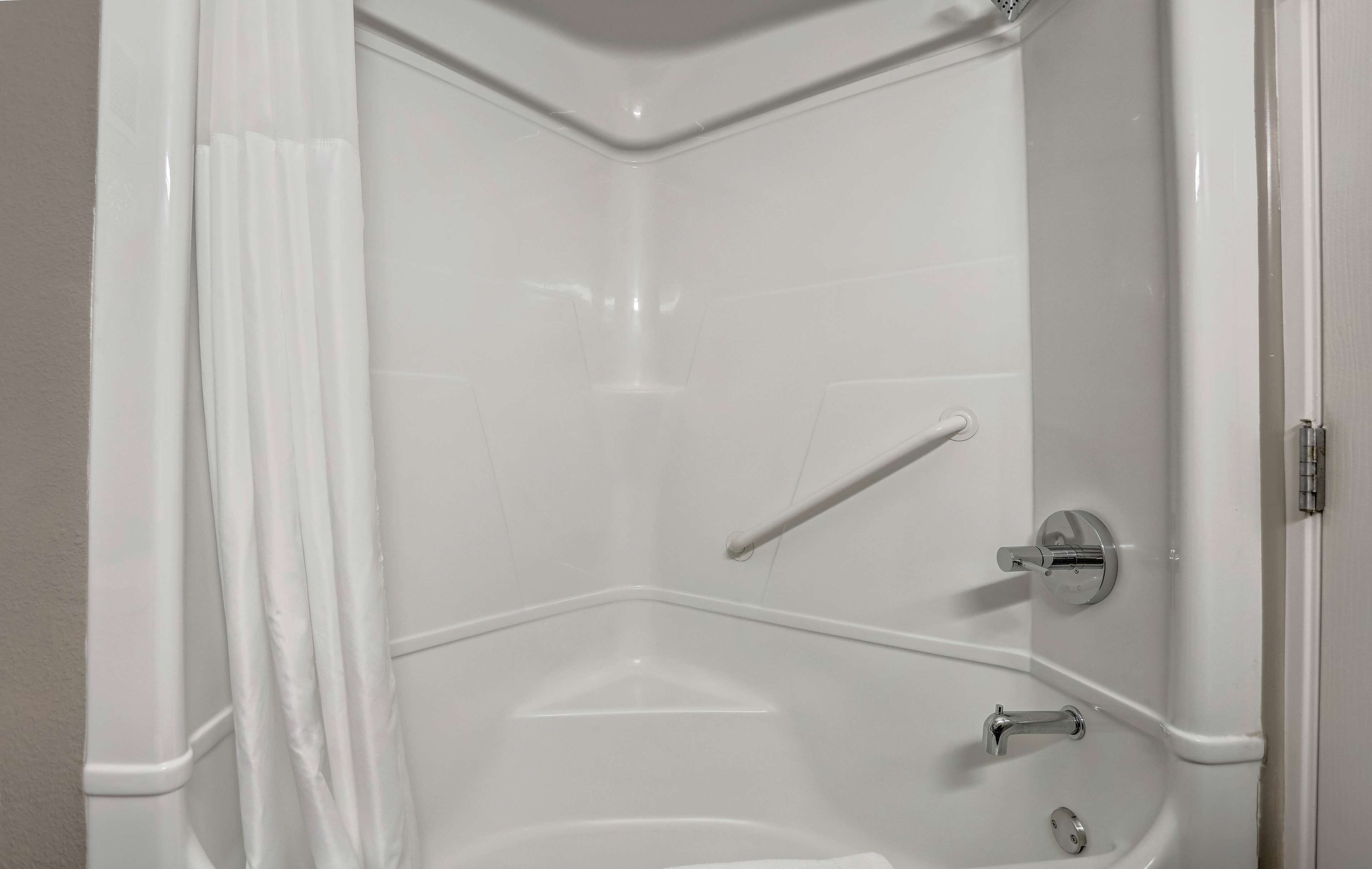 A corner shower with a white tiled wall, a shower curtain, a grab bar, and a handheld showerhead.