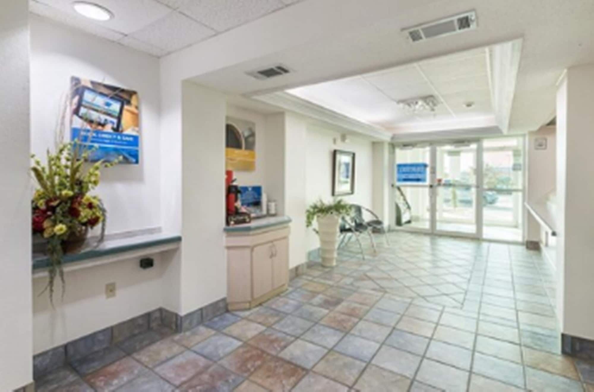 A spacious lobby with a tiled floor, a reception desk, a plant, and a glass door leading outside.