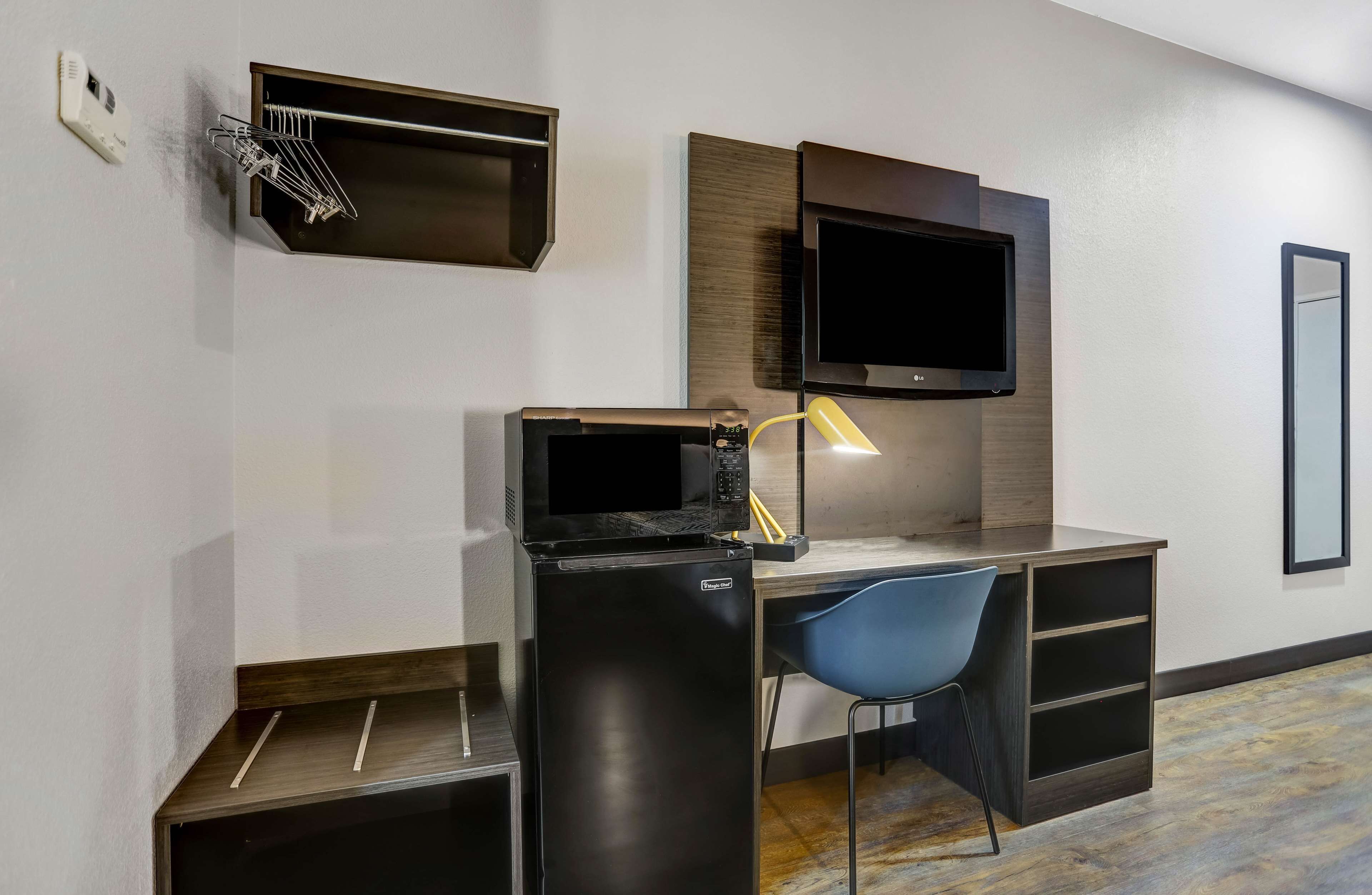 A modern hotel room with a desk, a microwave, a refrigerator, a TV, and a chair.