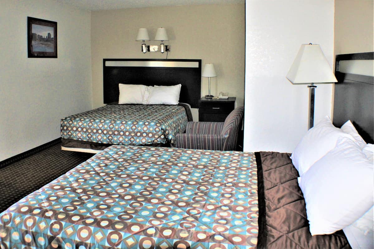 A hotel room with two beds, a nightstand, a lamp, and a framed picture on the wall.