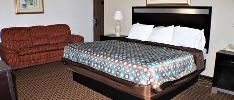 Una habitación de hotel con una cama grande, un sofá, una mesita de noche y una lámpara.