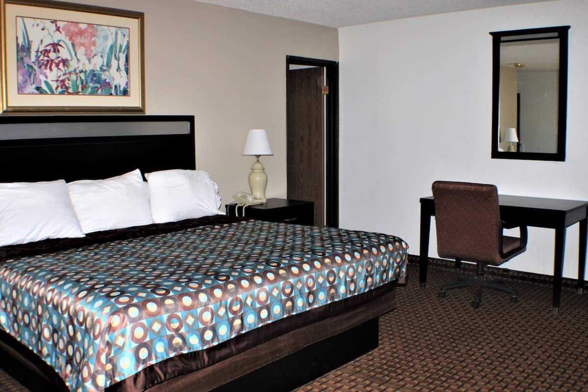 A hotel room with a large bed, a desk, a chair, a lamp, and a painting on the wall.