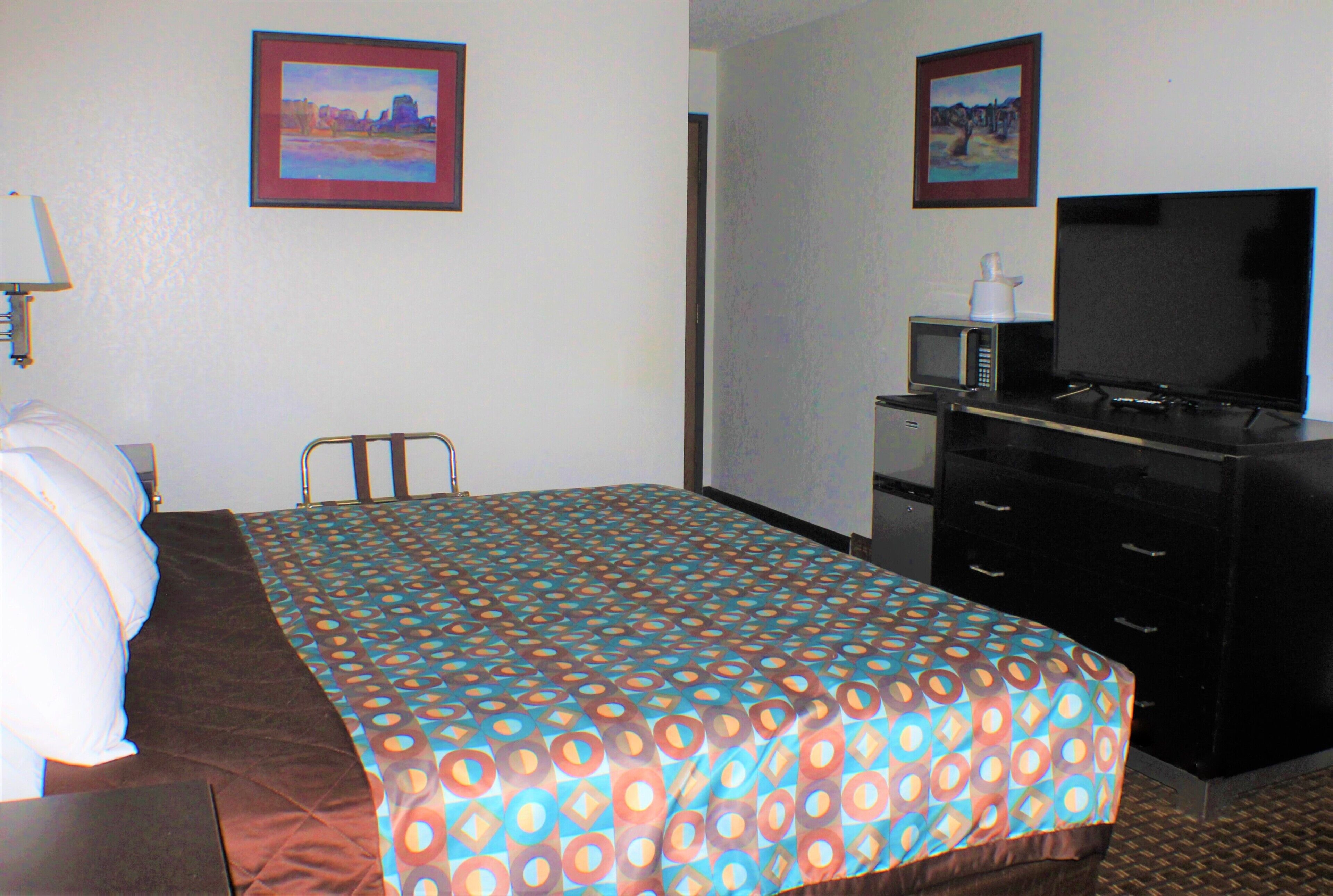 A hotel room with a bed, a desk, a television, and two framed pictures on the wall.