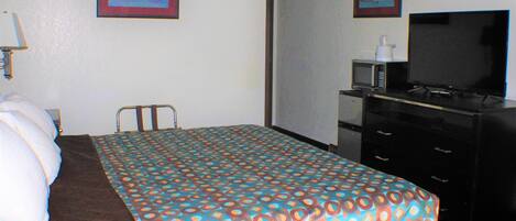 A hotel room with a bed, a desk, a television, and two framed pictures on the wall.
