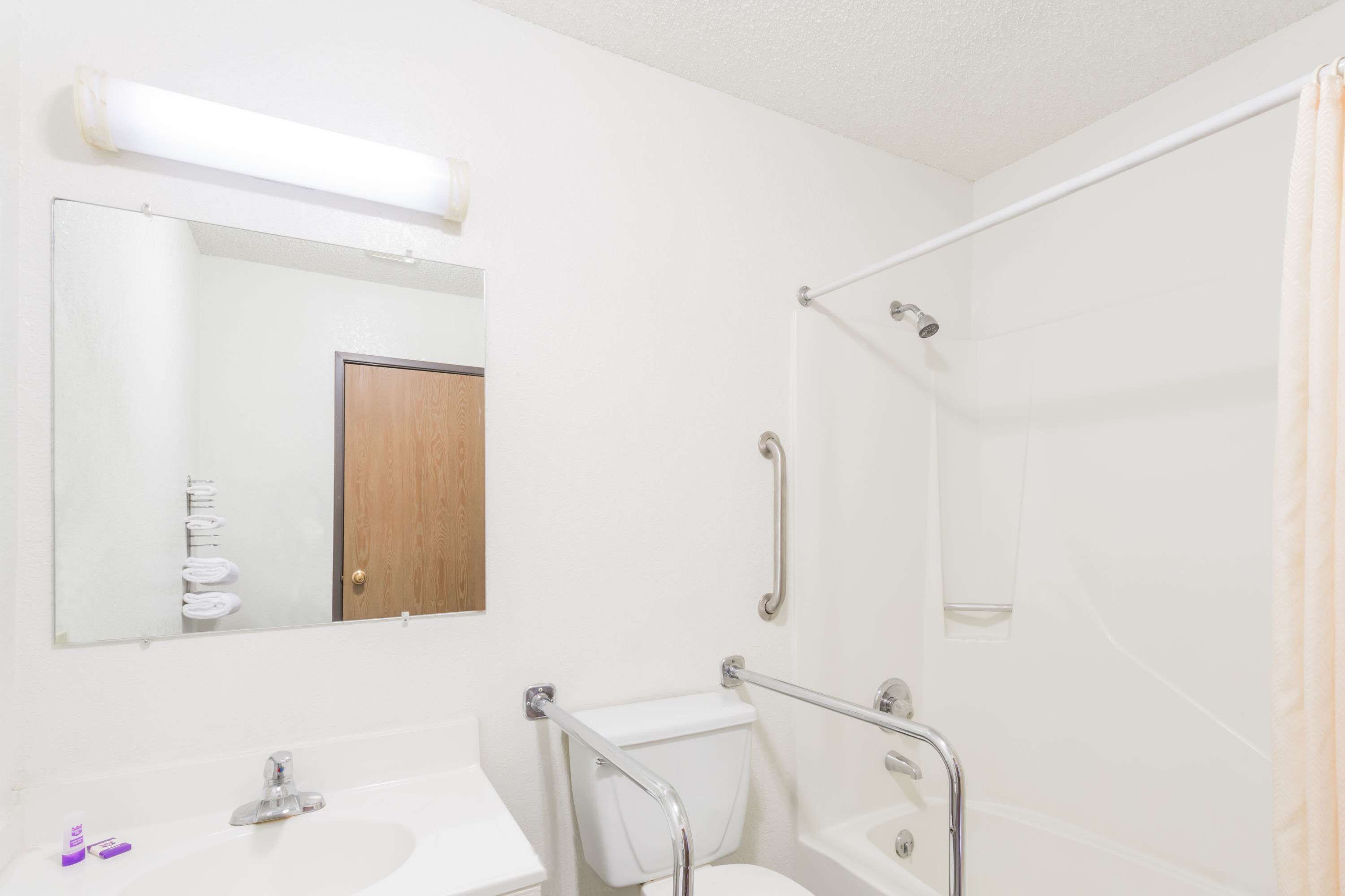 A bathroom with a white sink, mirror, and toilet. There is a shower with a glass door and a grab bar.