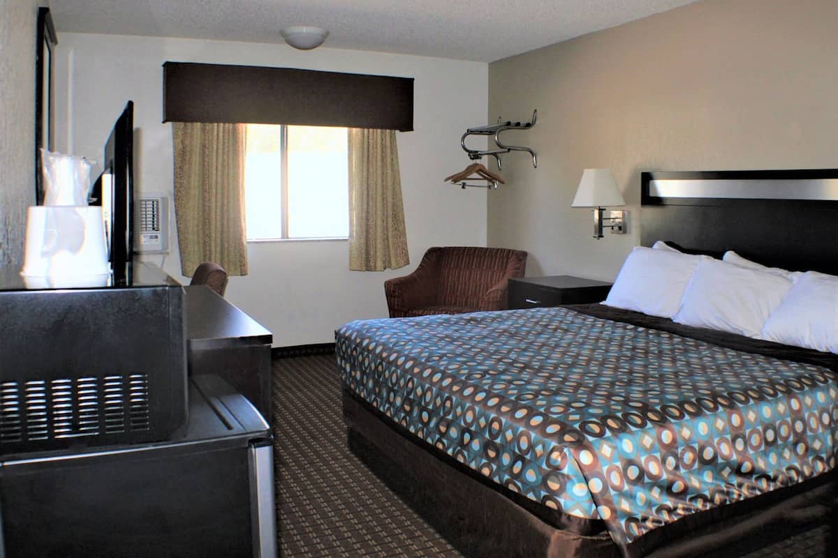 A hotel room with a bed, a desk, a chair, a TV, a lamp, and a window with curtains.