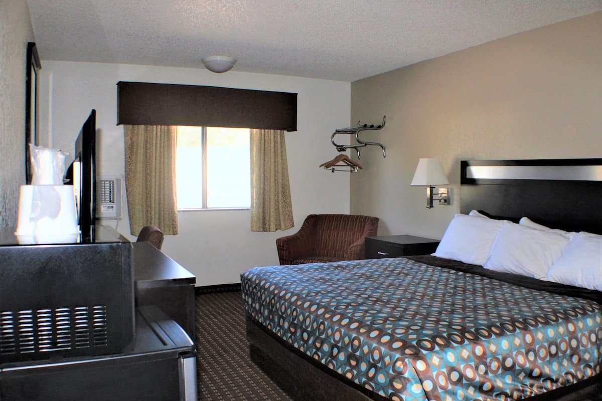 A hotel room with a bed, a desk, a chair, a TV, and a window with curtains.