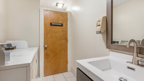 A bathroom with a wooden door labeled 'RESTROOM,' a white sink with a modern faucet, and a hand soap dispenser on the wall. - Red Roof Inn Greencastle South – Cloverdale (Cloverdale)