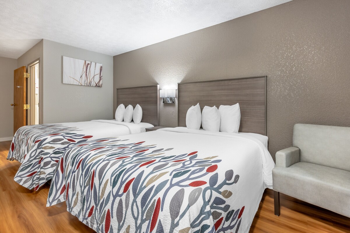 Une chambre d’hôtel avec deux lits, un canapé, une lampe fixée au mur et une porte.