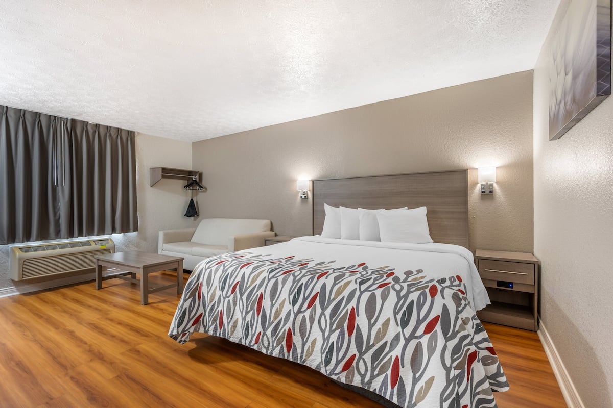 Habitación de hotel con cama, mesitas de noche, una silla, escritorio, calefactor y lámpara de pared.