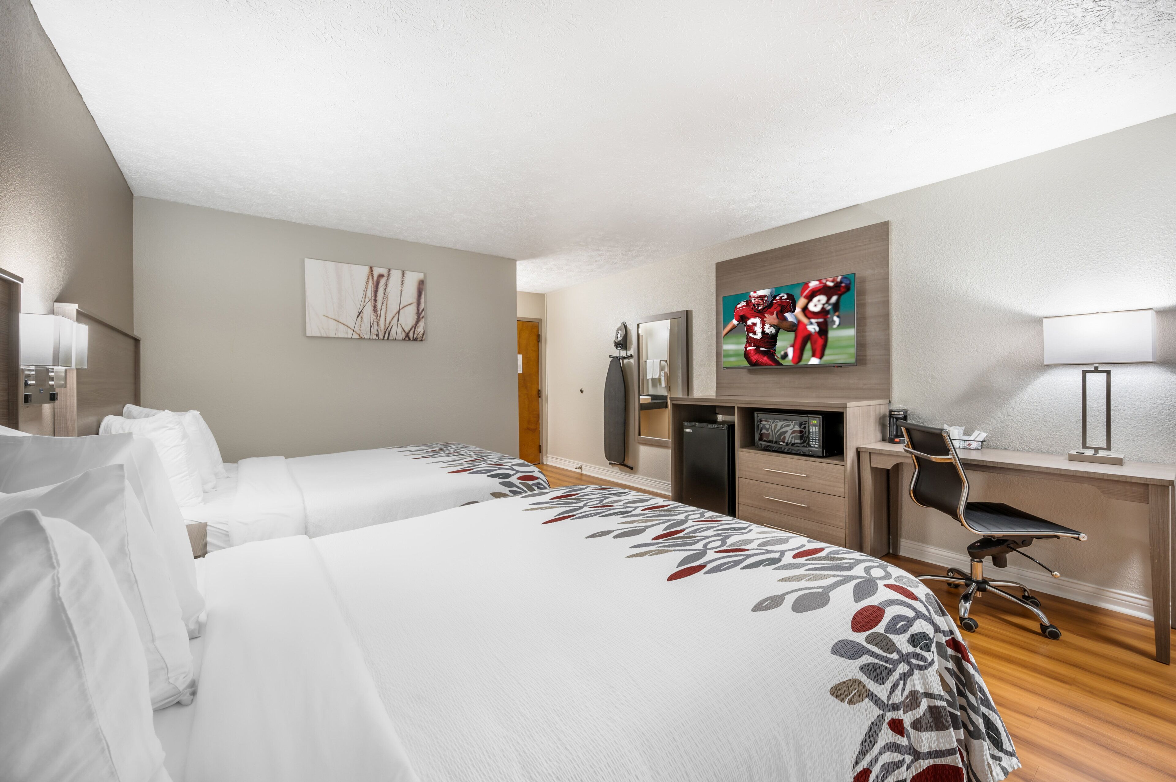 Une chambre d’hôtel avec deux lits, un bureau, une télévision et un réfrigérateur.