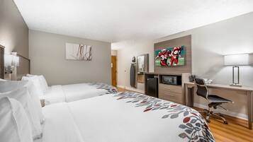 A hotel room with two beds, a desk, a television, and a refrigerator.