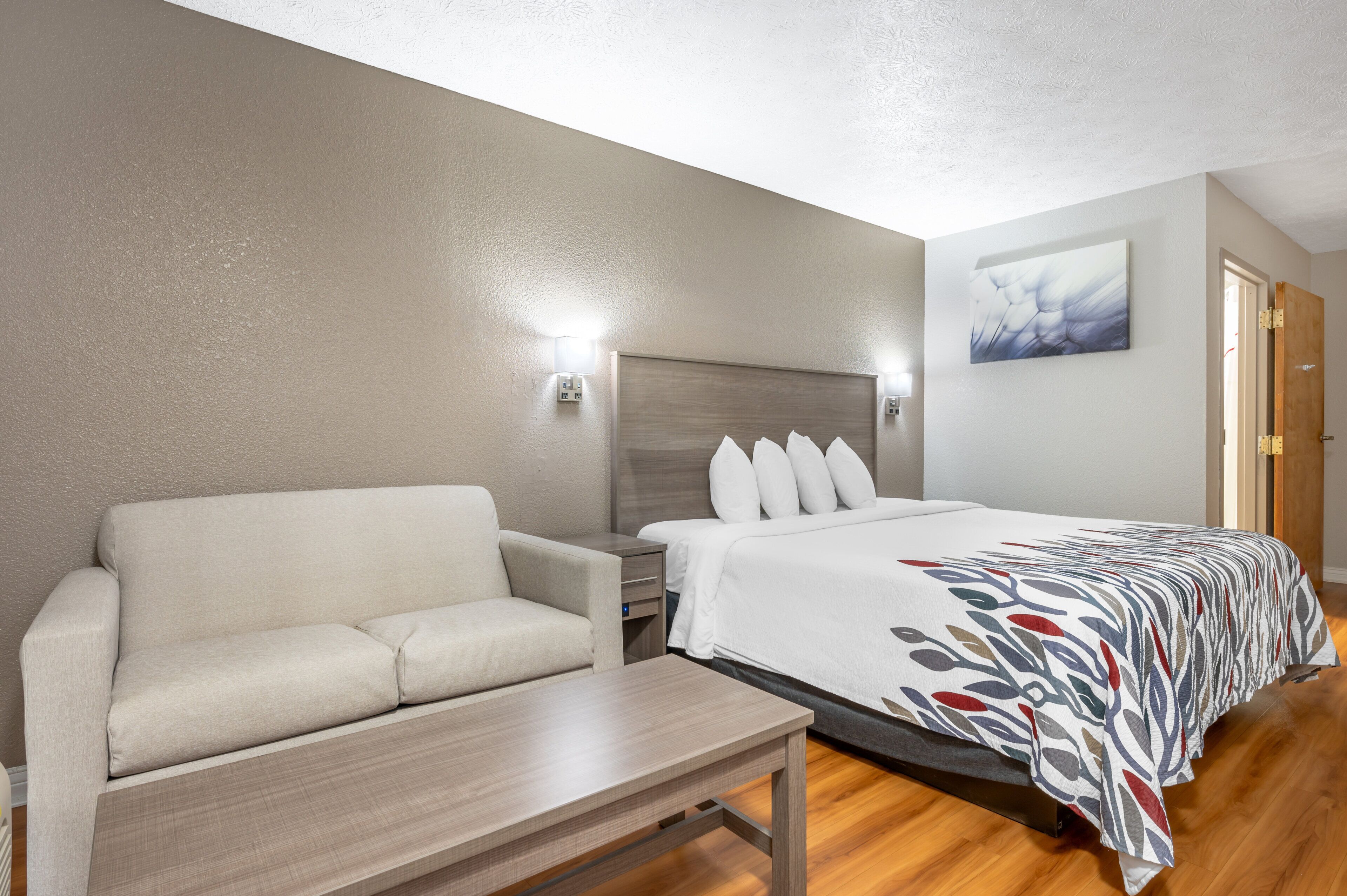 A hotel room with a bed, a sofa, a table, and a painting on the wall.