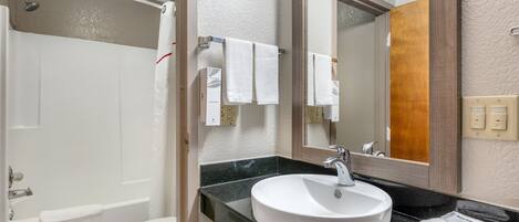 A bathroom with a bathtub, toilet, sink, and a large mirror.