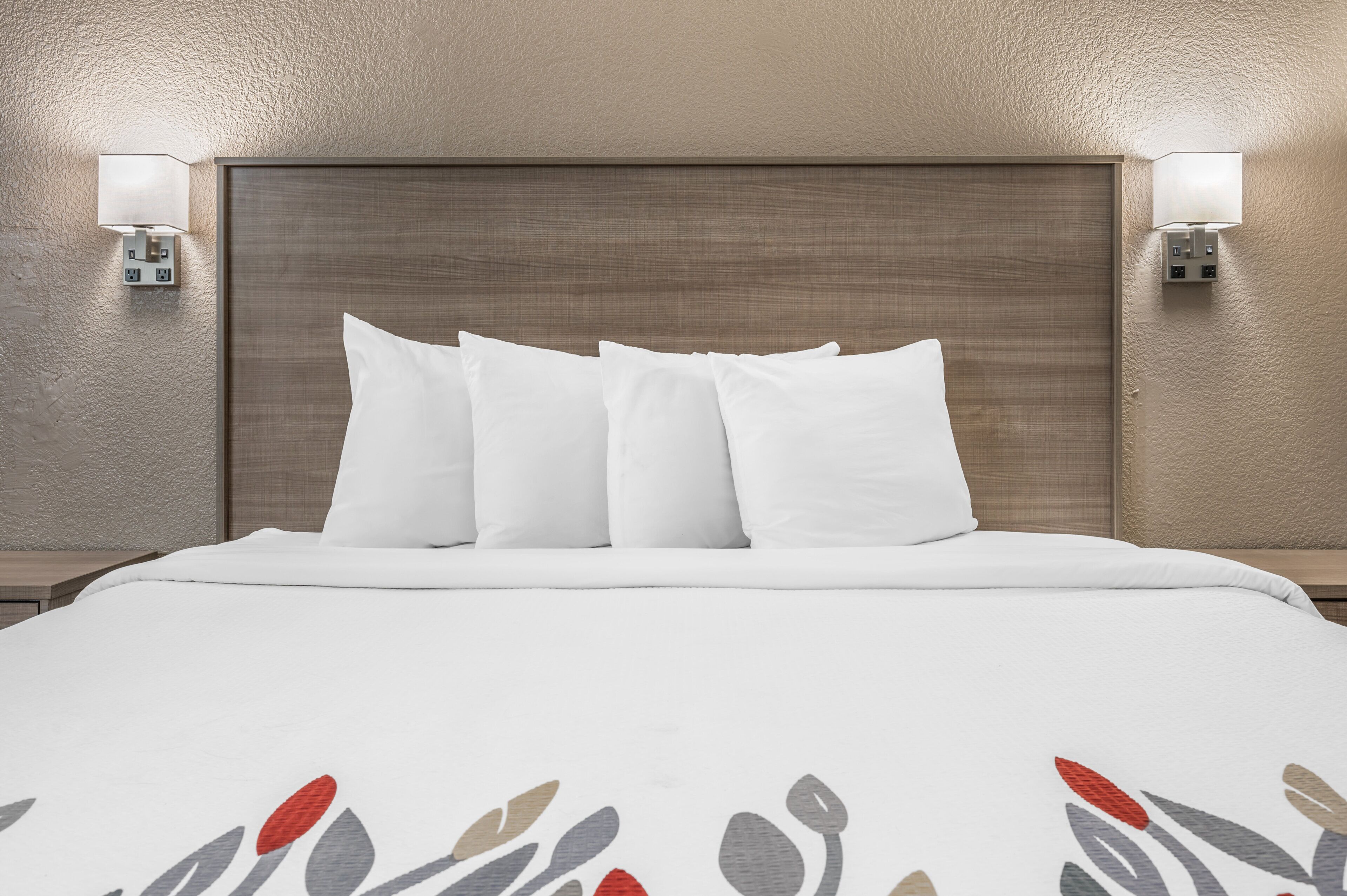 A hotel room with a large bed, a wooden headboard, and two wall-mounted light fixtures.