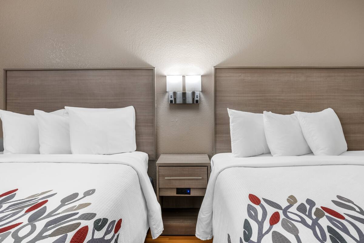 Habitación de hotel con dos camas, una mesita de noche con cajón y una lámpara fijada a la pared.