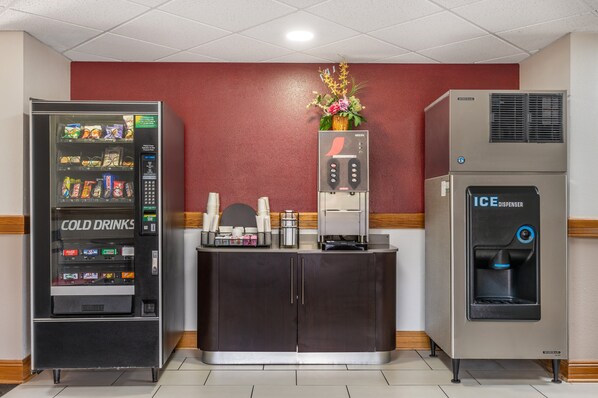 Un distributeur automatique portant l’inscription « BOISSONS FROIDES » et un autre distributeur à glace se trouvent dans une pièce dont un mur est rouge et qui contient un meuble en bois.