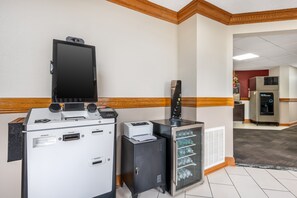 A reception area with a reception desk, a large flat-screen TV, a printer, a small cabinet, and a refrigerator. - Red Roof Inn Greencastle South – Cloverdale (Cloverdale)