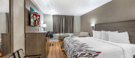 Une chambre d’hôtel avec un grand lit, un bureau, une chaise, une télévision et une fenêtre avec des rideaux.