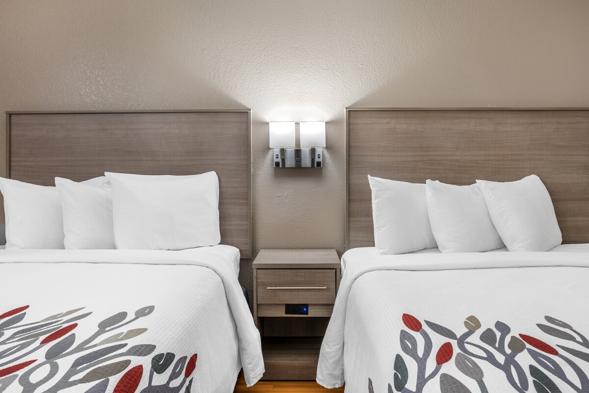 Une chambre d’hôtel avec deux lits, une table de chevet dotée d’un tiroir et un luminaire fixé au mur.