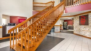 A hotel lobby with a wooden staircase, a reception desk, a Red Roof sign, and a vending machine. - Red Roof Inn Greencastle South – Cloverdale (Cloverdale)