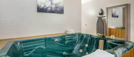 A spa room with a large green marble bathtub, a wooden vanity with a mirror, and a wall-mounted artwork.