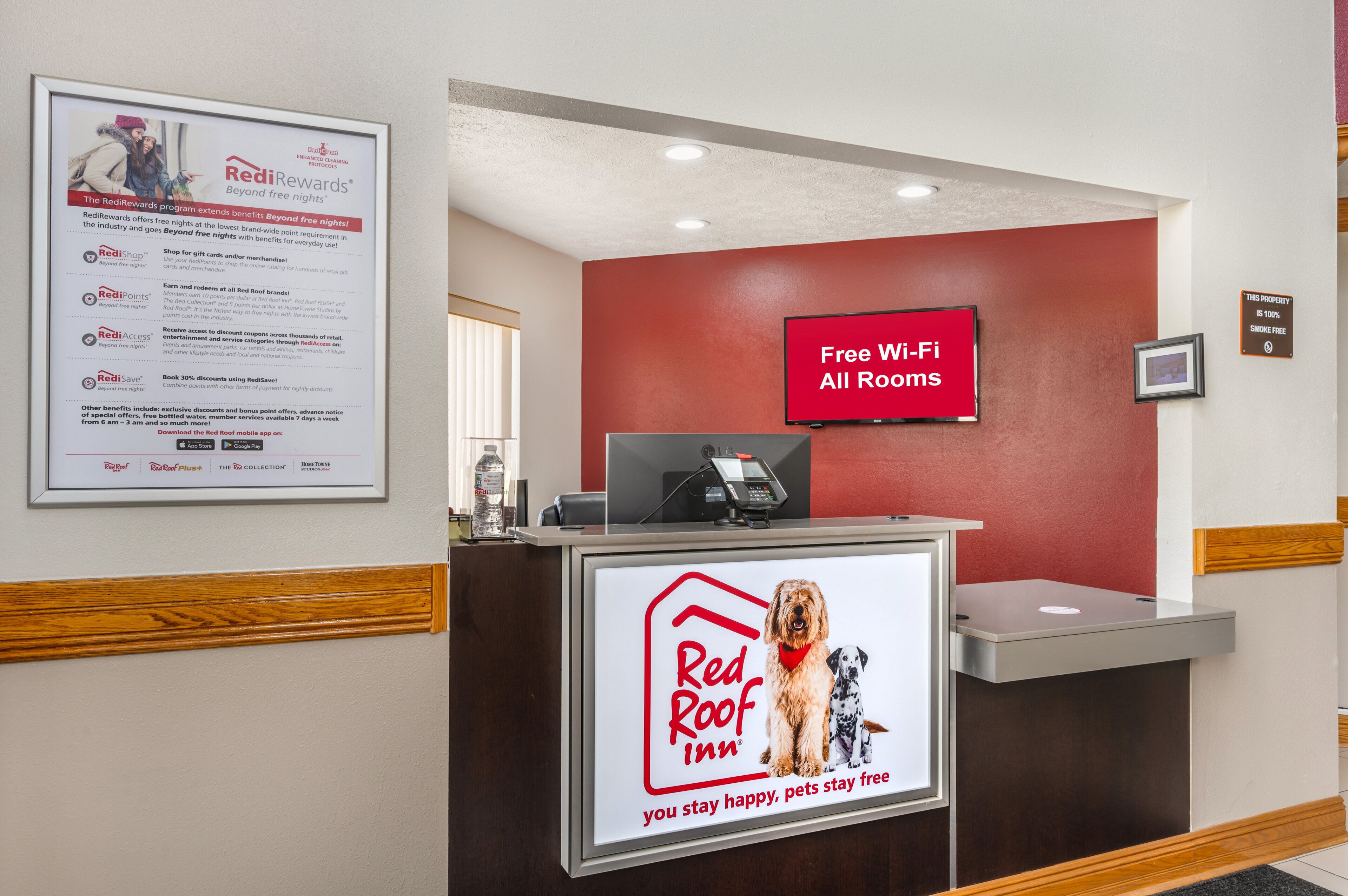 Un comptoir d’accueil d’un hôtel Red Roof Inn, avec une option de téléchargement de l’application mobile Red Roof, un panneau indiquant que les animaux de compagnie sont les bienvenus chez Red Roof, et un panneau Red Roof Plus.