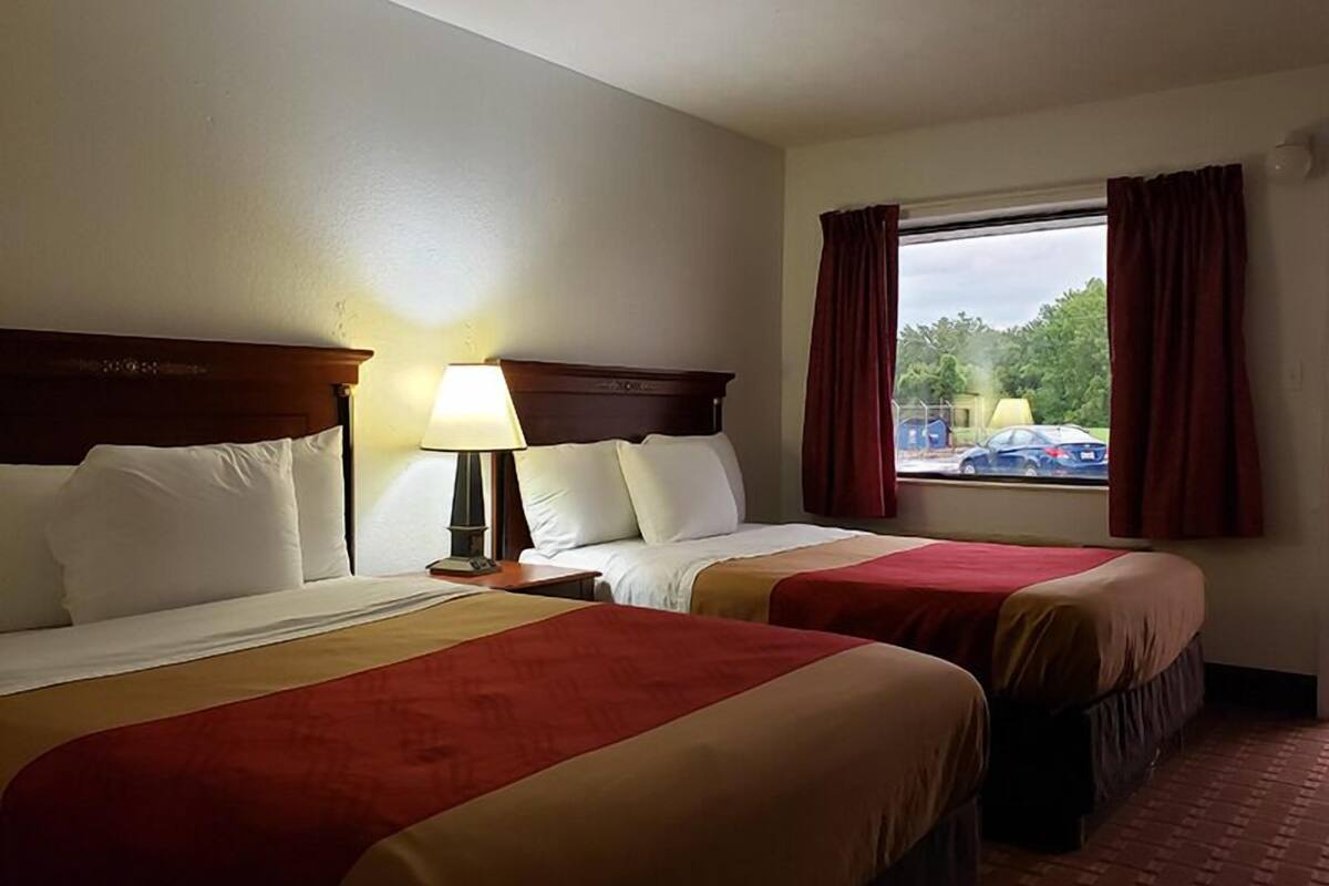 A hotel room with two beds, a nightstand with a lamp, and a window with curtains.